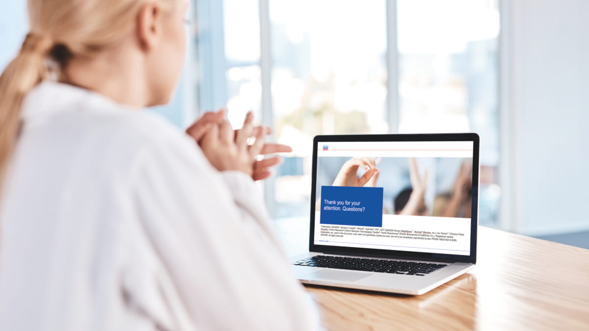 woman in lab coat looking at webinar on her laptop