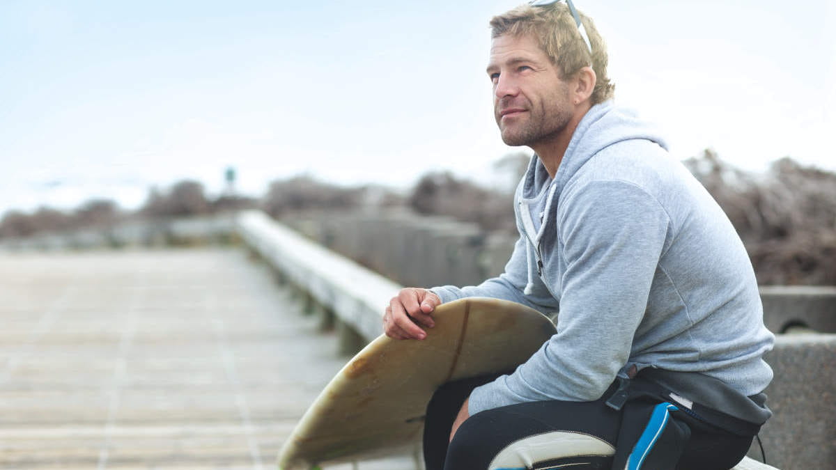 Man sitting with surfboard at the beach, evening, smile, satisfied, male, caucasian, QFT, QuantiFeron, TB testing, HIV
