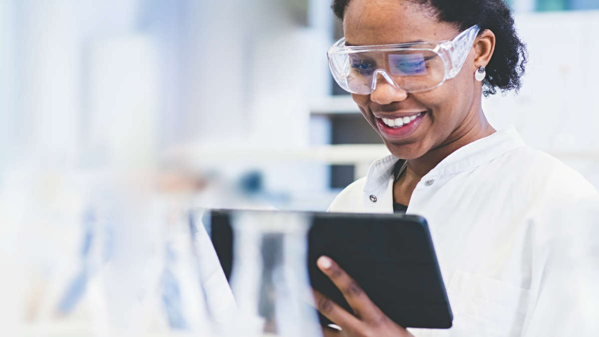 A woman in protective goggles holding a tablet in a lab
